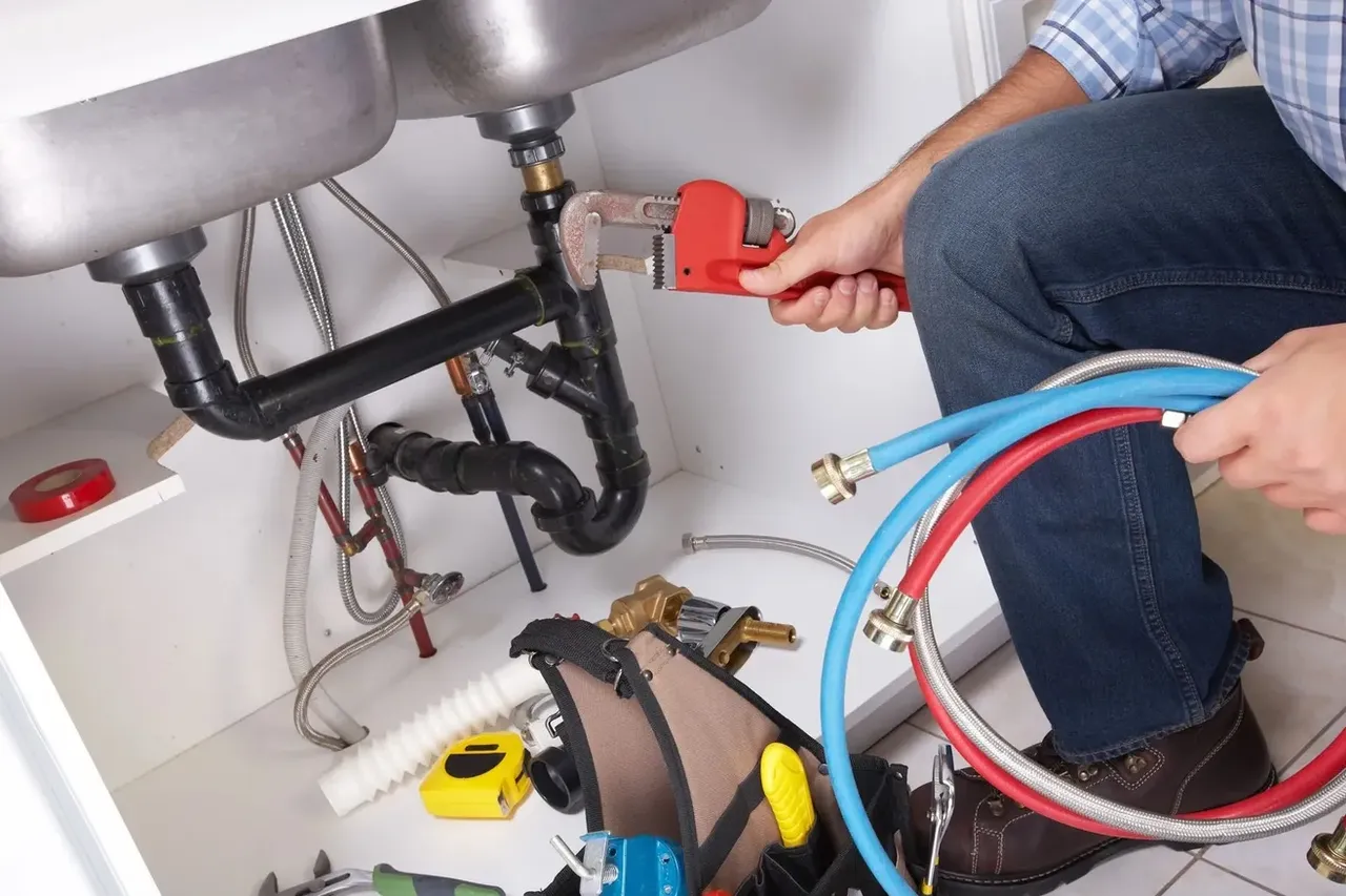 Plombier intervenant sur des raccords et un siphon sous un évier dans le 91